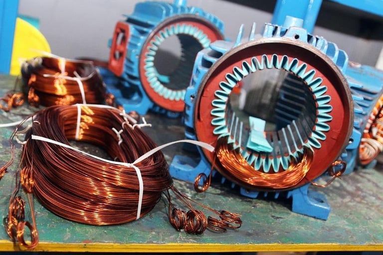 Electric motor components including copper wire coils and stator rings with red and blue motor casings in background