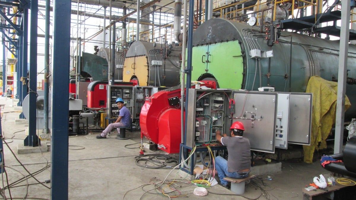 Industrial workshop showing red and yellow machinery parts, metal tanks, and electrical equipment under metal framework structures