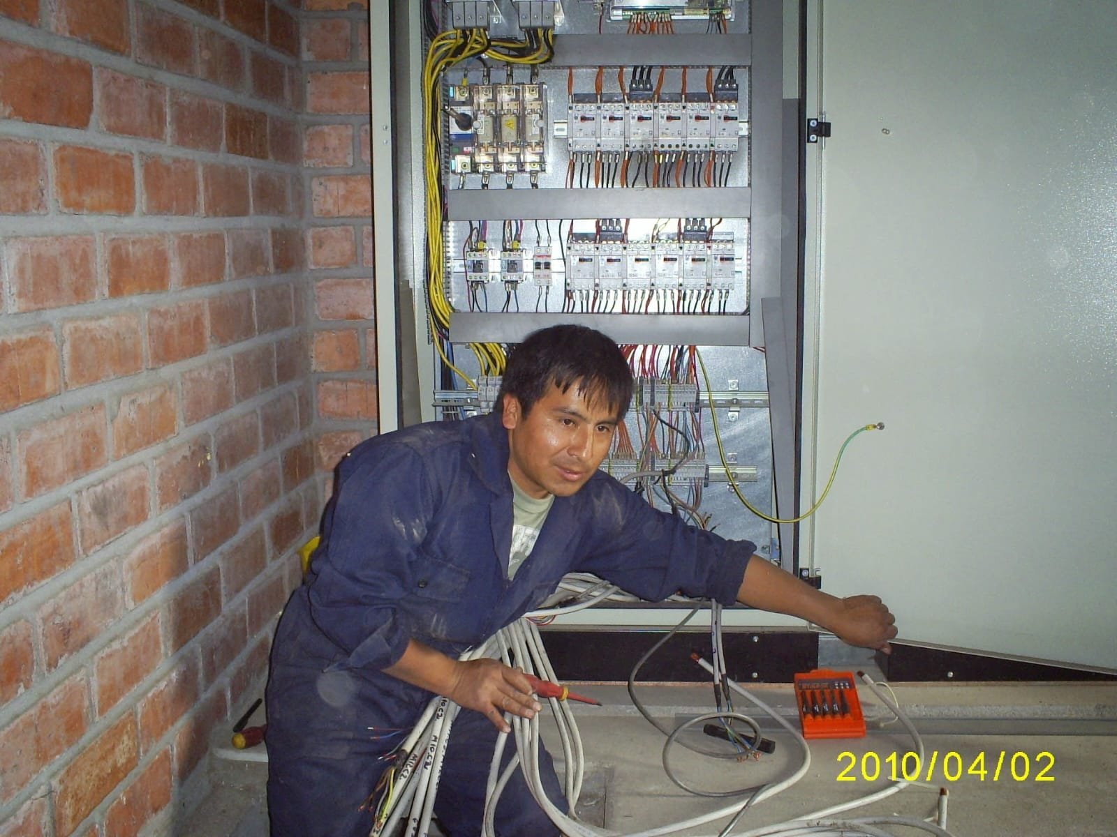 Technician in blue uniform working on electrical panel with wiring and cables