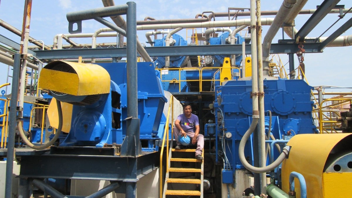 Worker on industrial drilling rig equipment with blue tanks and yellow components under clear sky